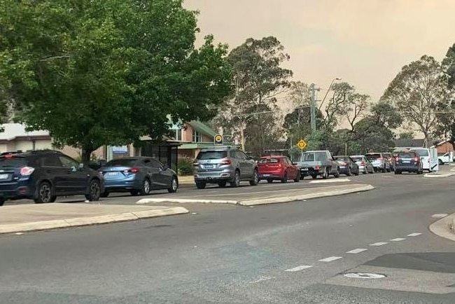A long line of cars queues on a street amid smoky skies.