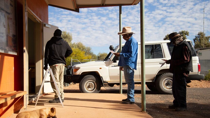 Three people stand in a line to vote in a remote community in the Northern Territory. 