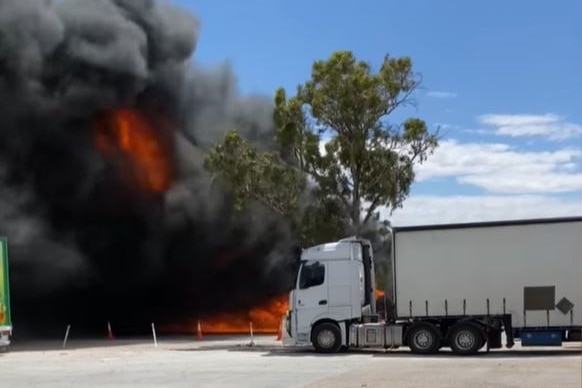 A white semi-trailer with flames and smoking coming from another truck behind it