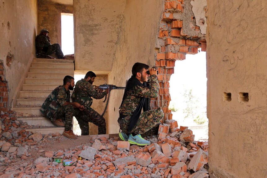 YPG fighters take up positions inside a damaged building in Syria as they monitor the movements of Islamic State
