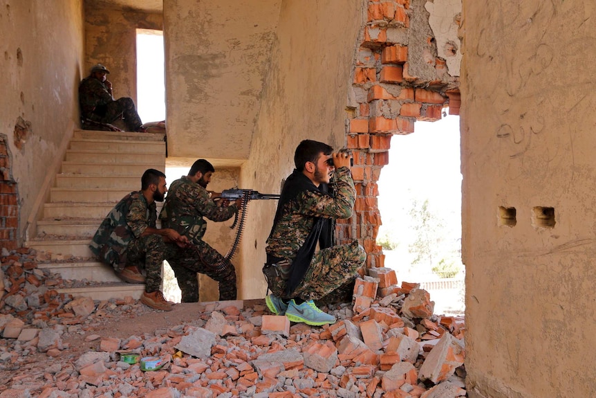 YPG fighters take up positions inside a damaged building in Syria as they monitor the movements of Islamic State