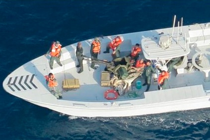 A group of men on a boat at sea are wearing orange life vests