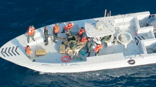 A group of men on a boat at sea are wearing orange life vests