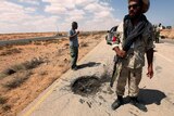 An anti-Gaddafi fighter surveys road damage caused by a pro-Gaddafi Grad missile in the Teassain area, 90 km east of Sirte.