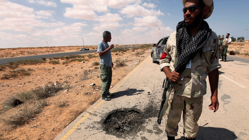 An anti-Gaddafi fighter surveys road damage caused by a pro-Gaddafi Grad missile in the Teassain area, 90 km east of Sirte.