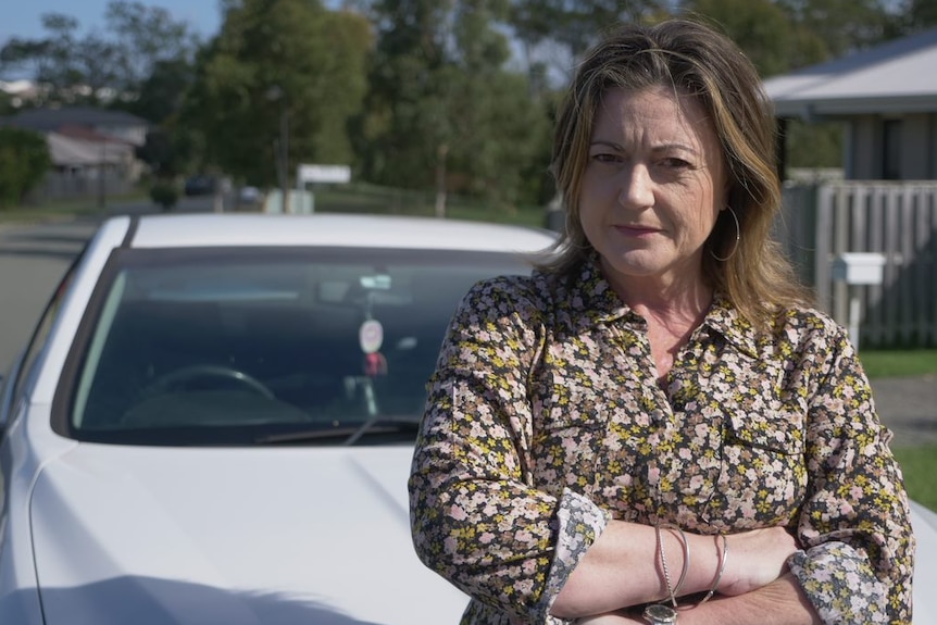 A woman with crossed arms leaning on her car.