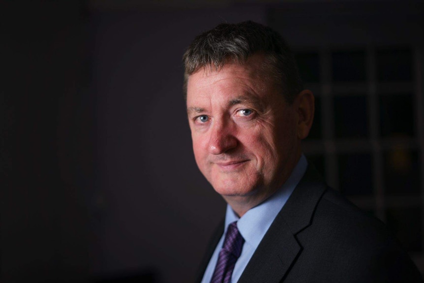 A man wearing a suit and a muted smile.