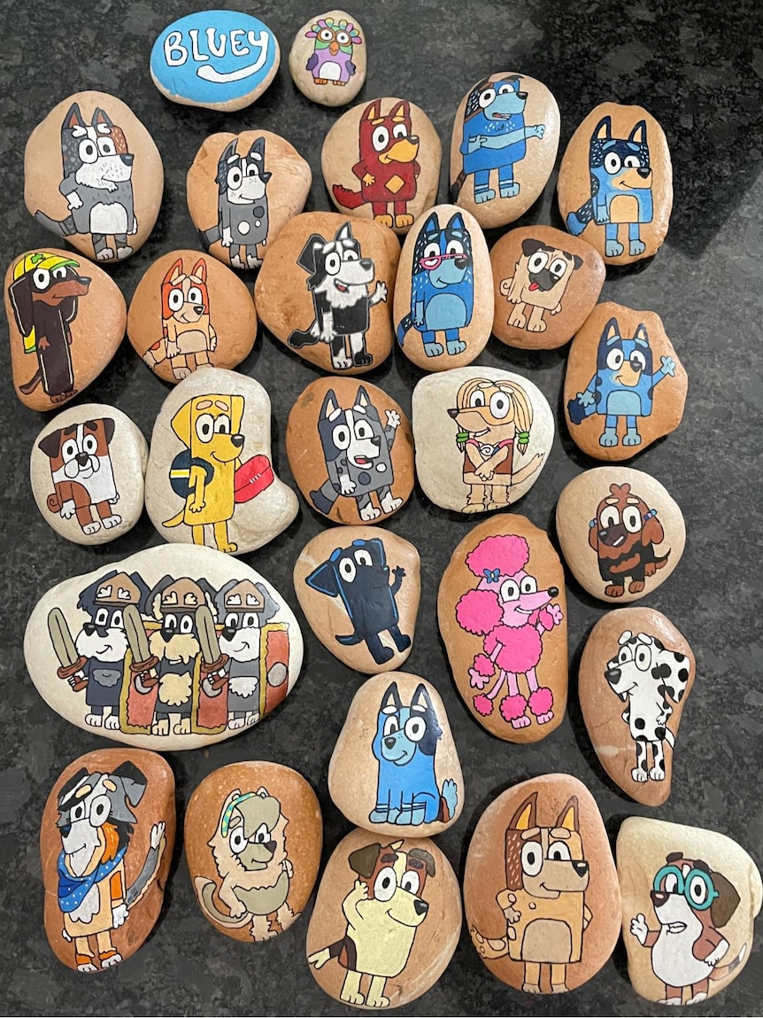 A dozen painted rocks depicting illustrations of Bluey characters. 
