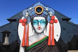 The colourful mural against a blue sky. It features a Russian lady in Chinese dress with a Balinese headdress.