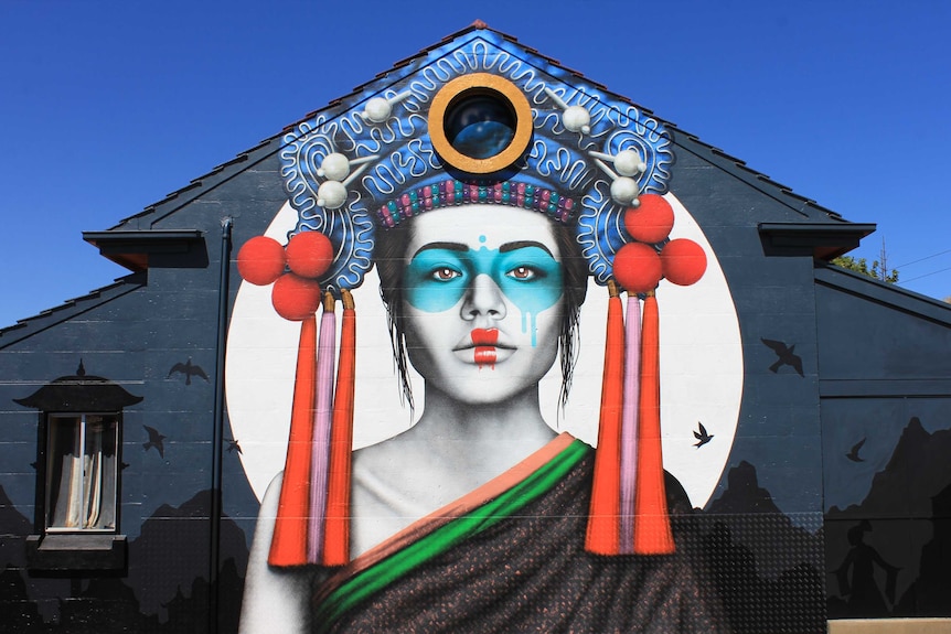The colourful mural against a blue sky. It features a Russian lady in Chinese dress with a Balinese headdress.