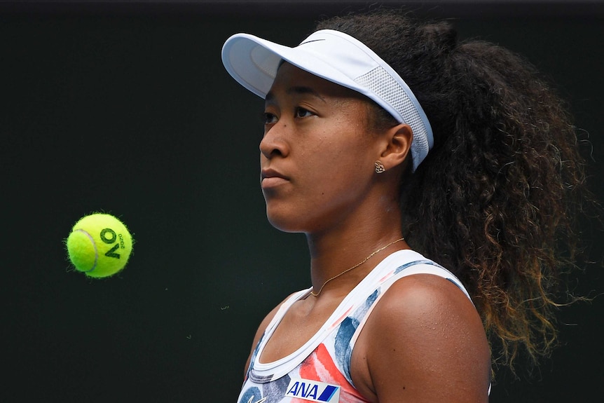 A female tennis player looks straight ahead as a tennis ball bounces next to her at the Australian Open.