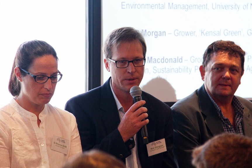 A man holds a microphone and sits with two other industry representatives at an event in Sydney.