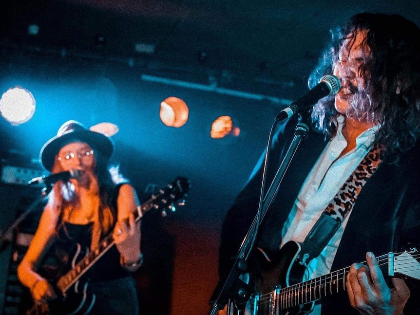 Two musicians with long hair playing guitars and singing