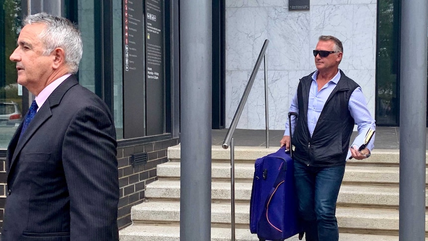 two men walk down the stairs of a court house, carrying suitcases