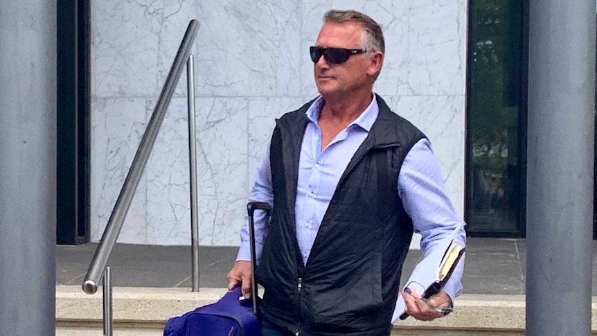 two men walk down the stairs of a court house, carrying suitcases