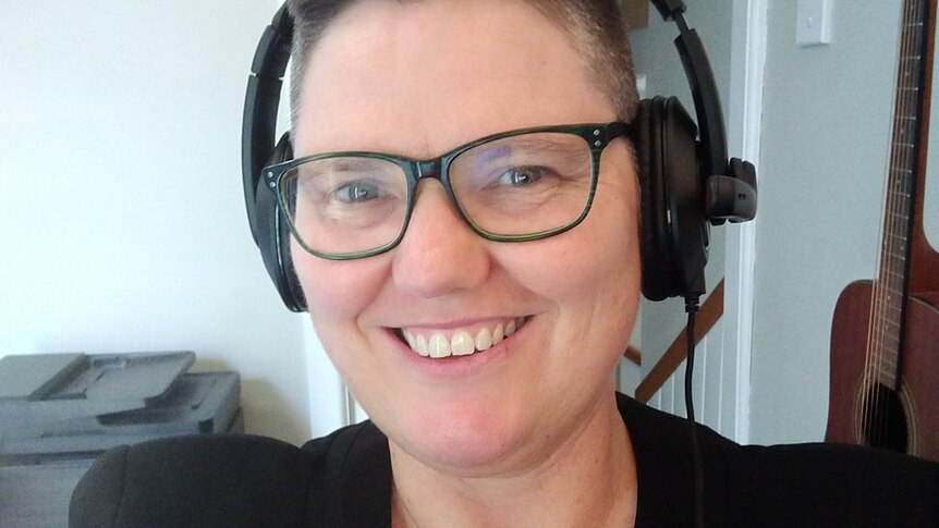 A woman with cropped hair wears glasses and heaphones while smiling.