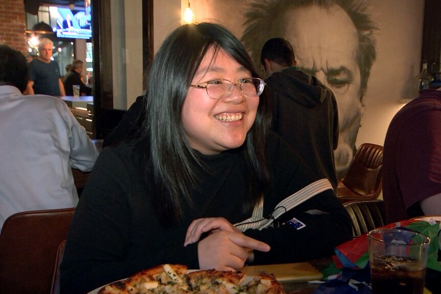 A woman with glasses smiles while sitting at a table in a pub.