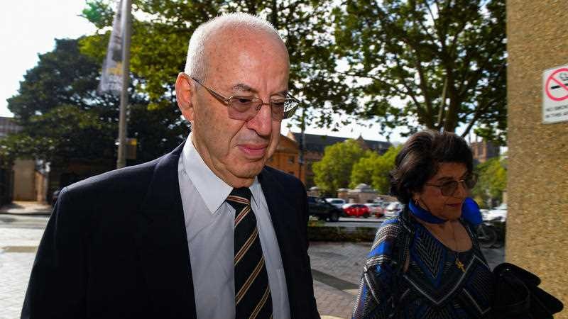 A man with glasses looking grim walking into court.