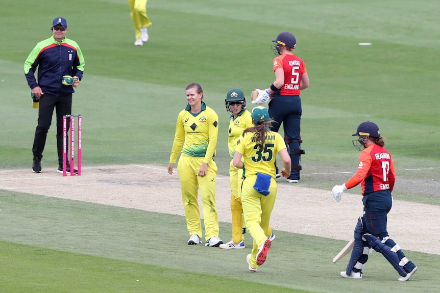 Cricketers celebrate a wicket as the dismissed batter walks off.
