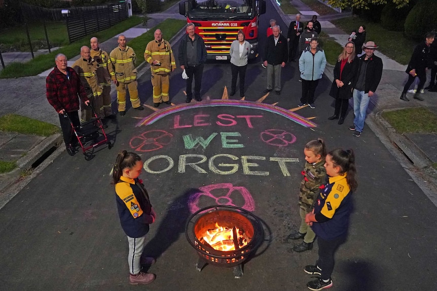 a group of people in firefighters stand in a street with lest we forget written in chalk