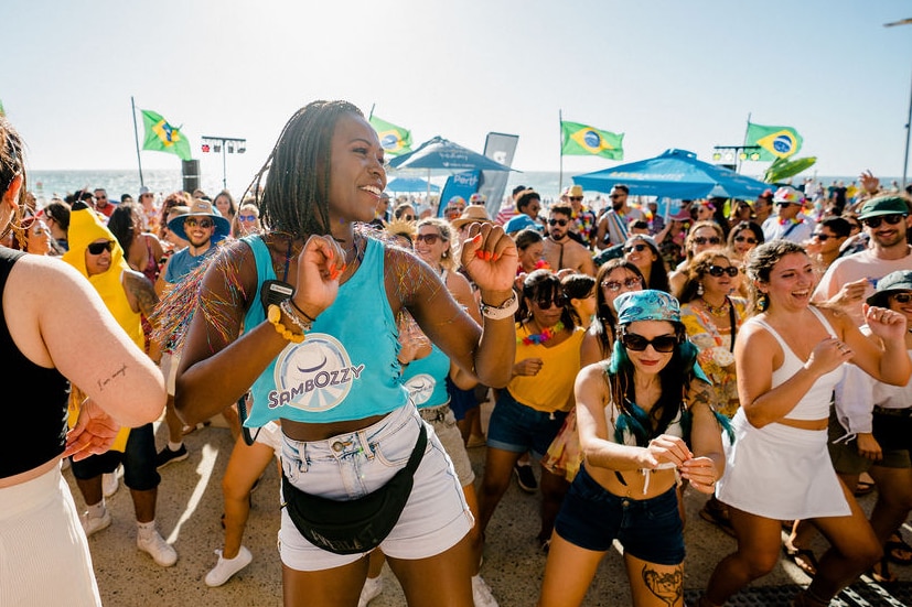 Une femme vêtue d'un maillot bleu et d'un short en jean danse avec une foule derrière elle.