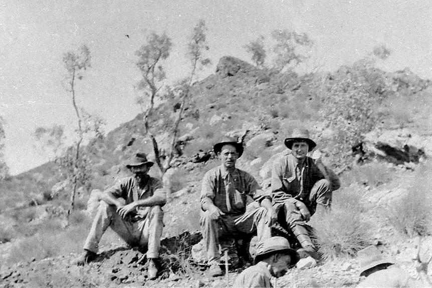 A black-and-white image of a group of prospectors relaxing on a hillock.