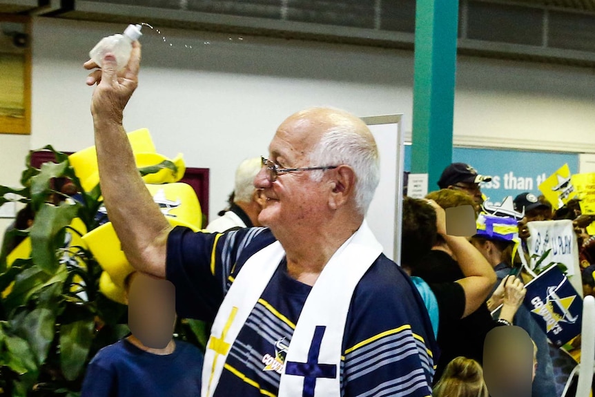 Father Dave Lancini blesses the crowd of supporters and the players as the Cowboys at Townsville airport