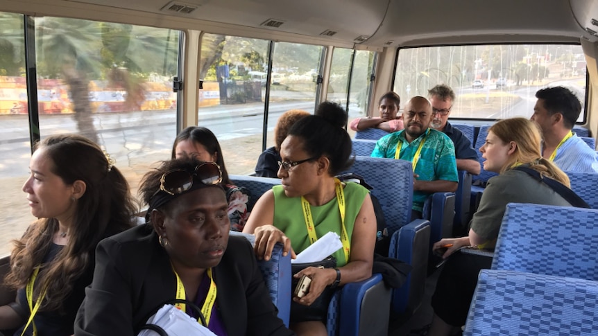 A bus carries members of the local PNG and international media. All are wearing lanyards.