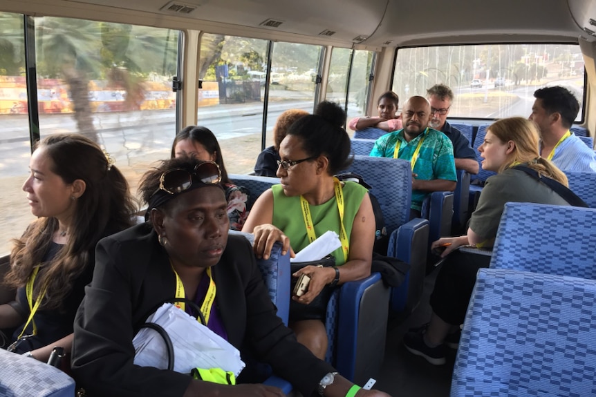 A bus carries members of the local PNG and international media. All are wearing lanyards.