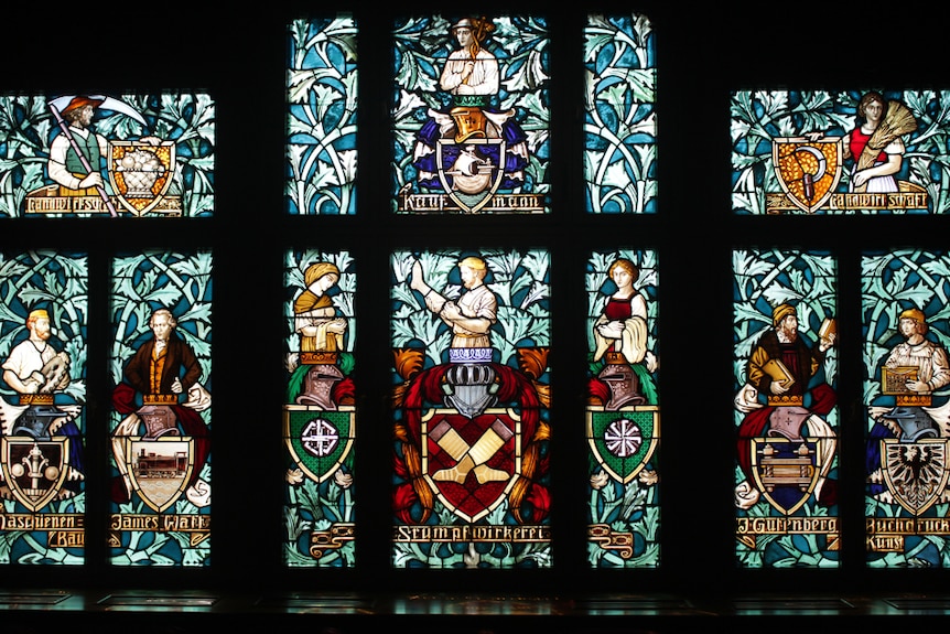 Stained-glass window panes featuring human characters and German writing.