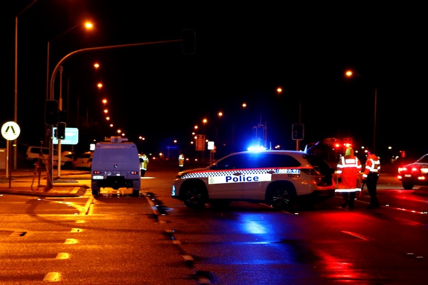 A police car is parked at night across an intersection where two vehicles crashed.