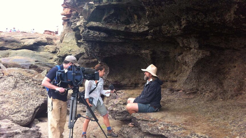 Erin Parke holding microphone interviewing man about dinosaur bones while cameraman films.