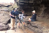 Erin Parke holding microphone interviewing man about dinosaur bones while cameraman films.