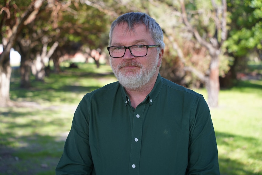 Mark Glasson standing in a park with trees in the background.