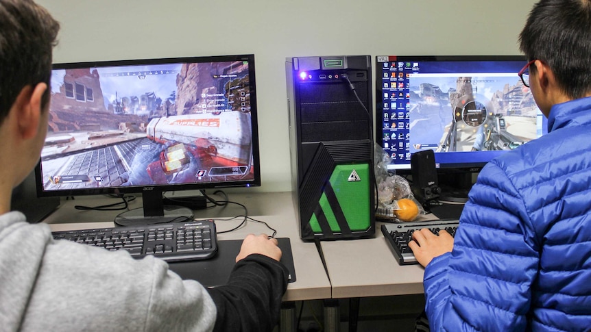 Over the shoulder shot of two boys playing computer games on PCs.