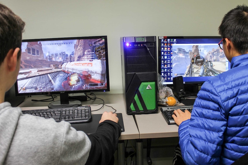 Over the shoulder shot of two boys playing computer games on PCs.