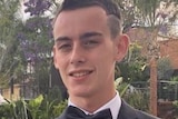 A teenage boy smiles for a photo while wearing a suit.