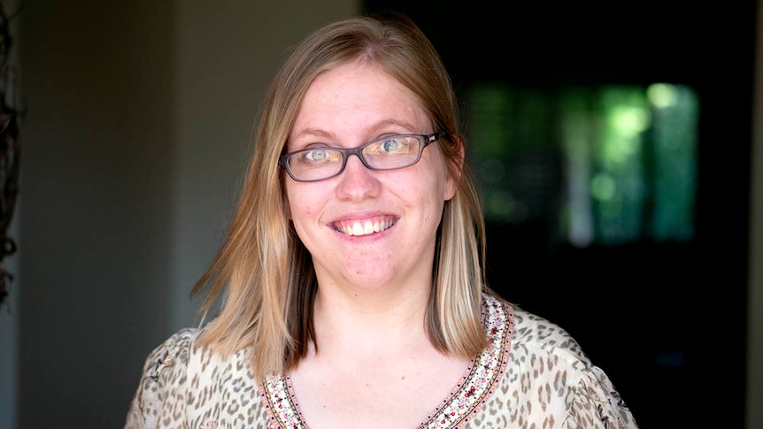 A woman wears glasses and smiles at the camera.