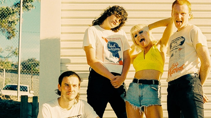 Faded photo of rock band Amyl & The Sniffers. Frontwoman Amy Taylor has her tongue poking out.