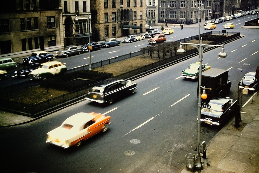 An old photo of a new york avenue in 1955 with old cars and taxis going by