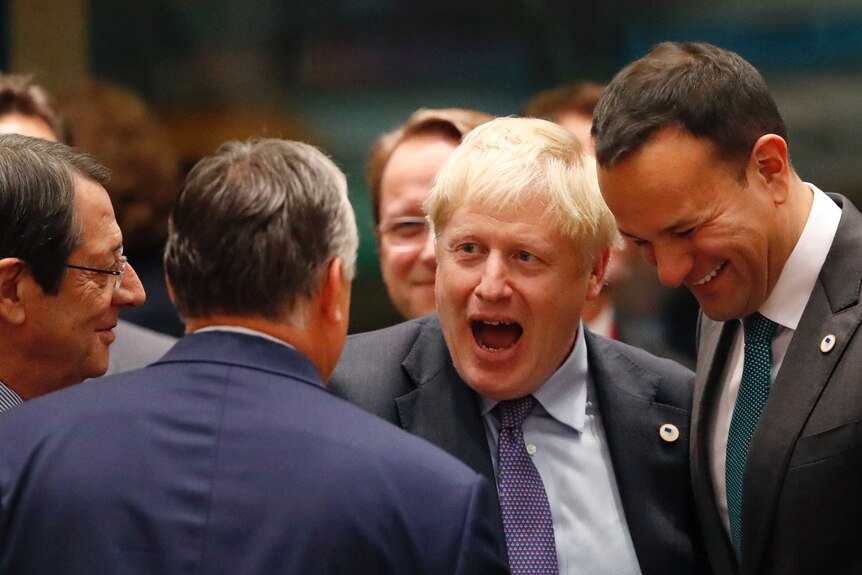 Boris Johnson smiling surrounded by men in suits