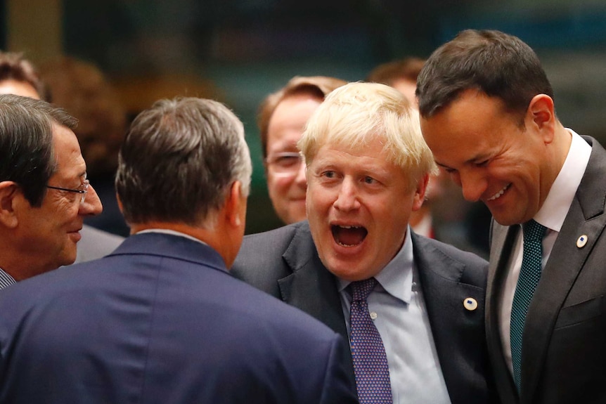 Boris Johnson smiling surrounded by men in suits