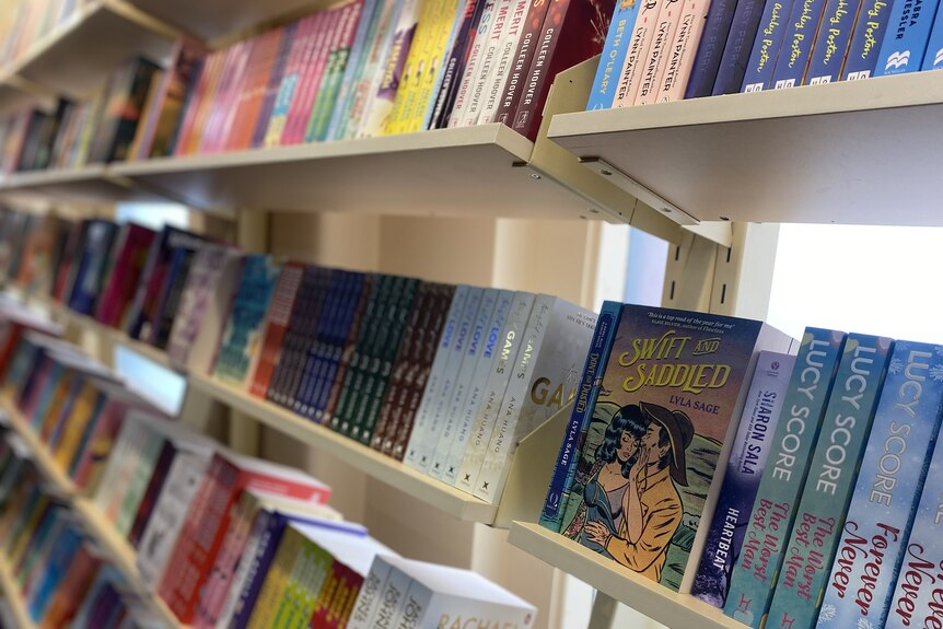 a book shelf displays rows of romance books. 