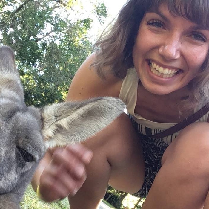 Gitta Scheenhouwer crouches down next to a kangaroo and smiles at the camera.