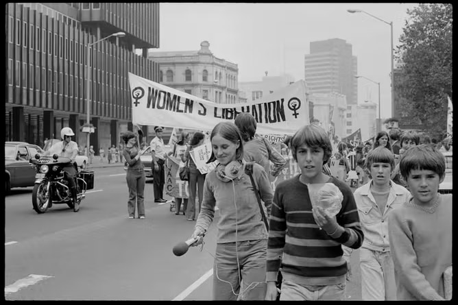 black and white photo of protestors walking under a women's liberation sign