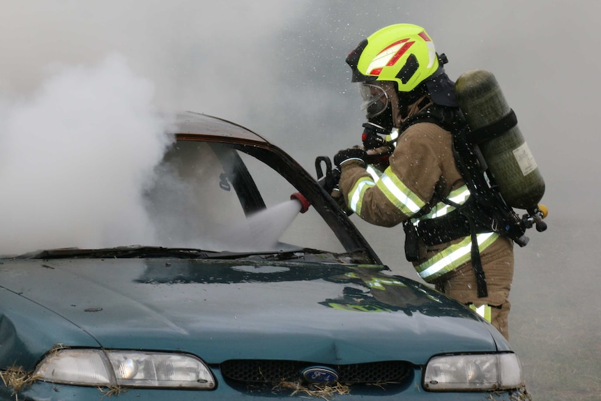 A female firefighter sprays firefighting foam into a smoking car.