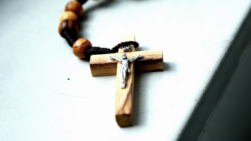 A wooden crucifix on rosary beads sits on a table.