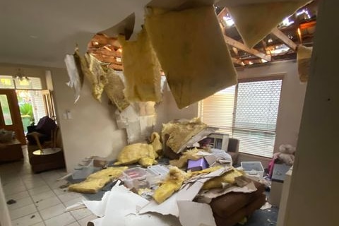 A home's roof fallen through with debris in the lounge room.