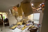 A home's roof fallen through with debris in the lounge room.