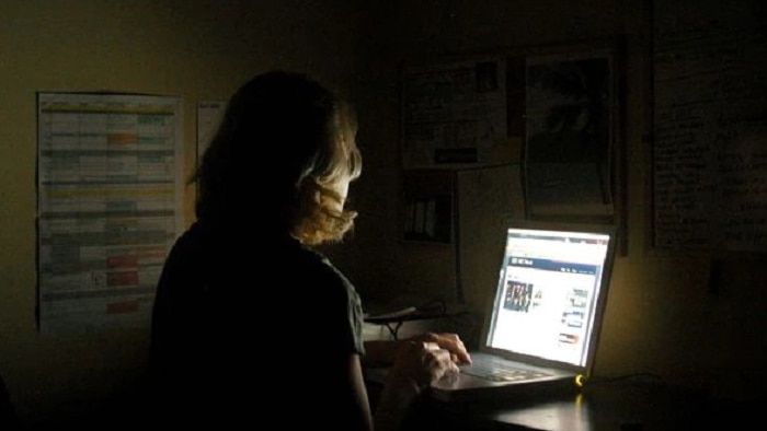 A woman sits at a computer in the dark.